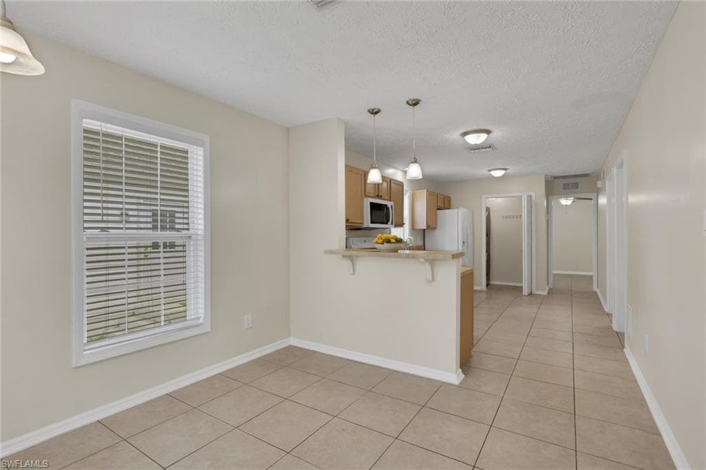 Open-concept living area with tile flooring, a kitchen featuring wood-finish cabinetry, and a breakfast bar