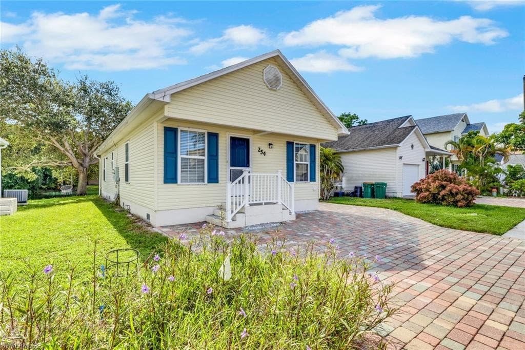 Siding exterior with blue window shutters, front porch with white railing, and a paver driveway