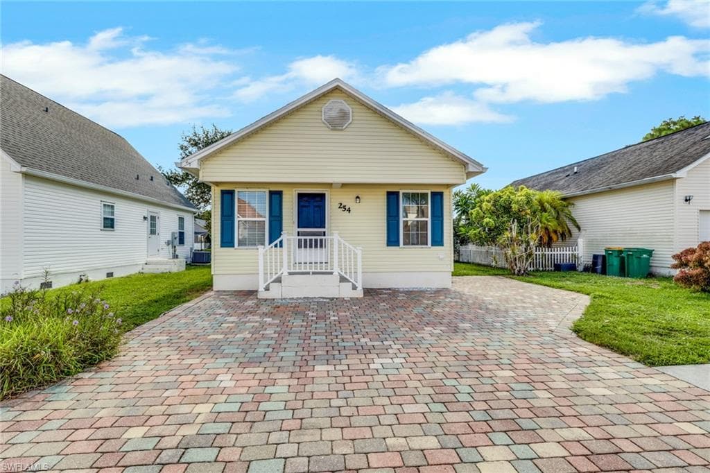 Charming cottage-style residence featuring a cream-colored exterior with blue shutters and trim, complemented by a covered front porch with white railings and columns