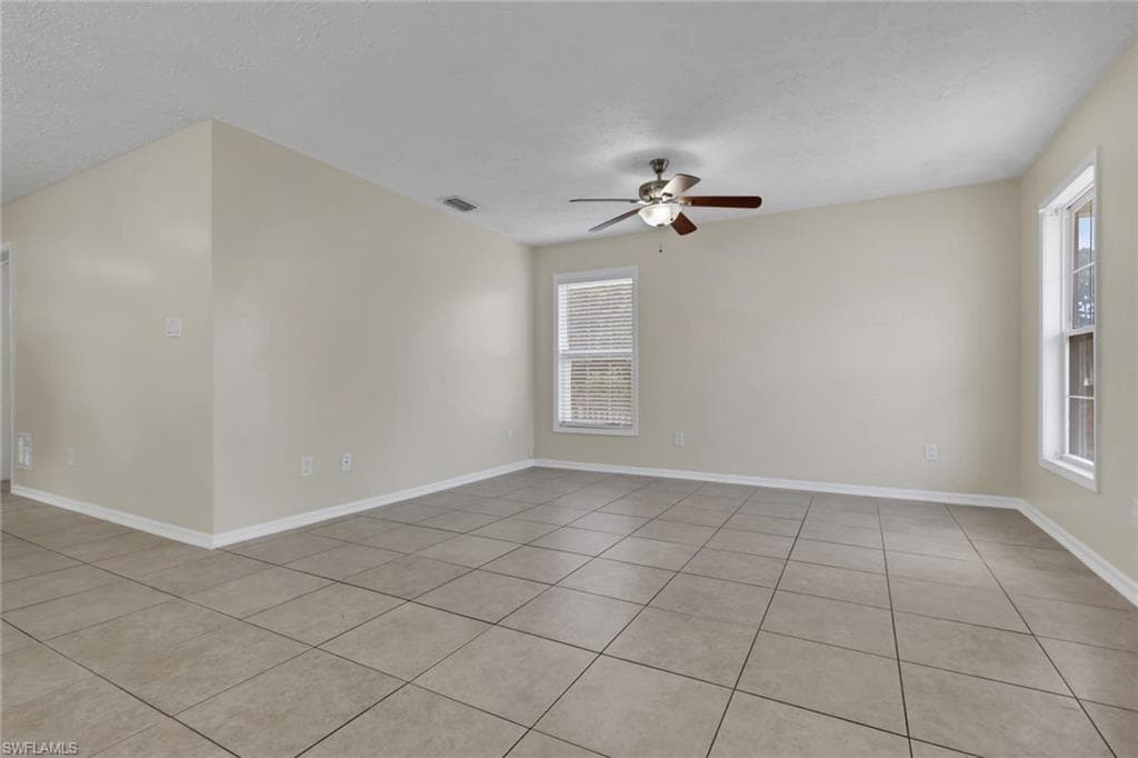 Spacious room featuring neutral tone walls, tile flooring, multiple windows, and a ceiling fan with integrated lighting