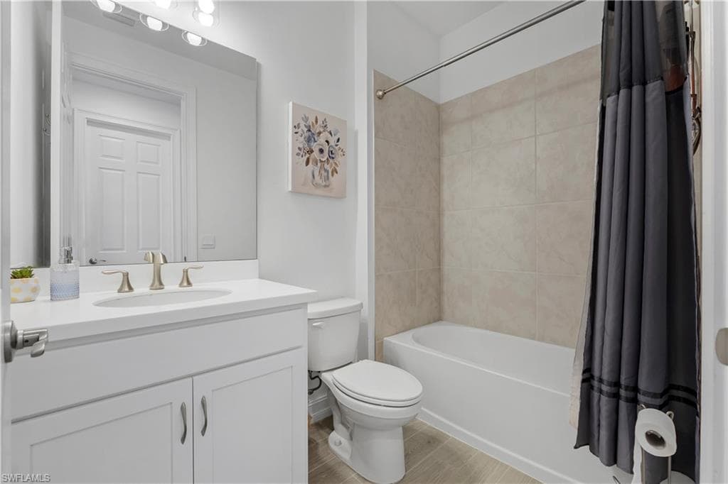 Modern bathroom featuring a white vanity with dual sink configuration and brushed nickel fixtures, large framed mirror with integrated lighting, white ceramic toilet, and a soaking tub with tile surround and coordinating gray shower curtain