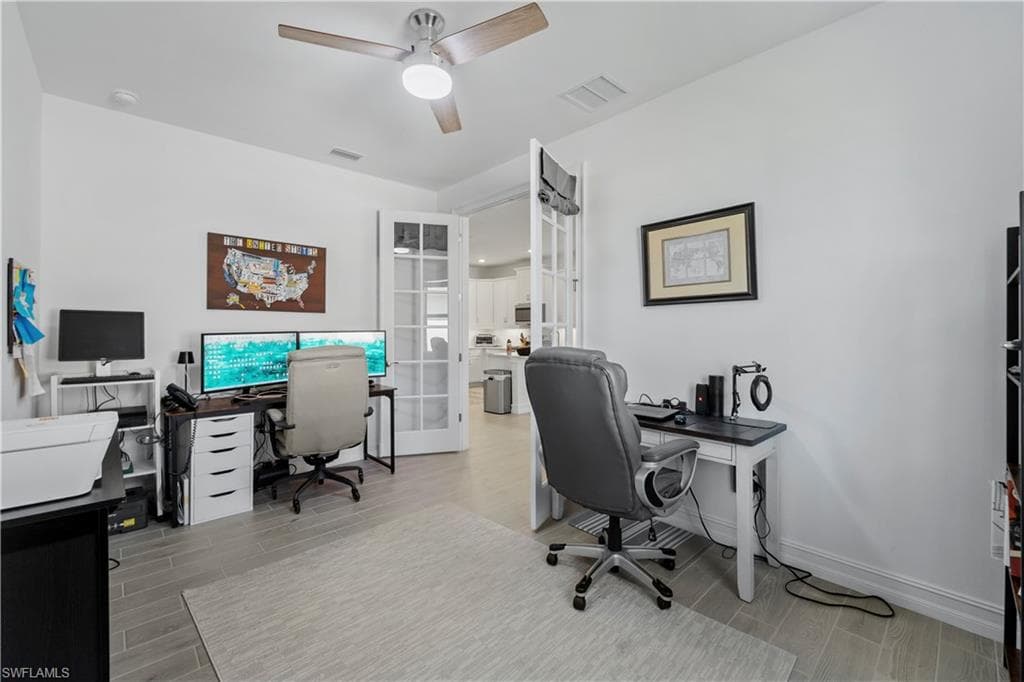 Spacious room featuring wood-finish tile flooring, a ceiling fan with integrated lighting, and French doors