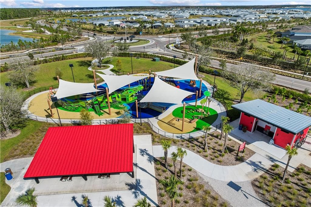 Expansive community park featuring a playground with shade canopies, a vibrant mural, a covered picnic area, and a red-sided amenity building