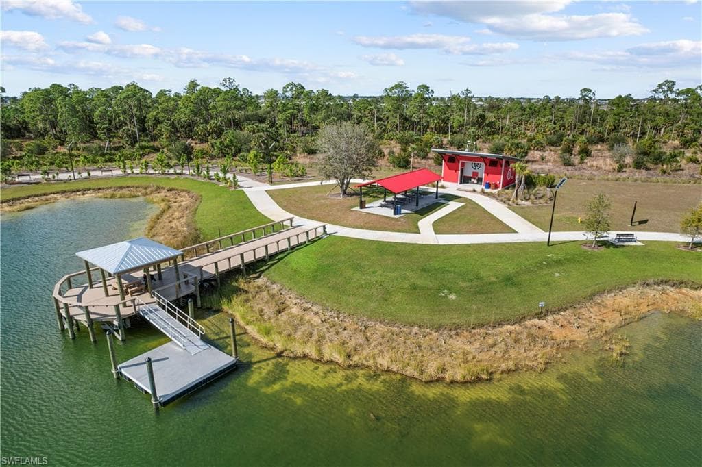 Waterfront pier with a covered seating area, floating dock, paved pathways, and a red recreational building with an attached covered picnic area