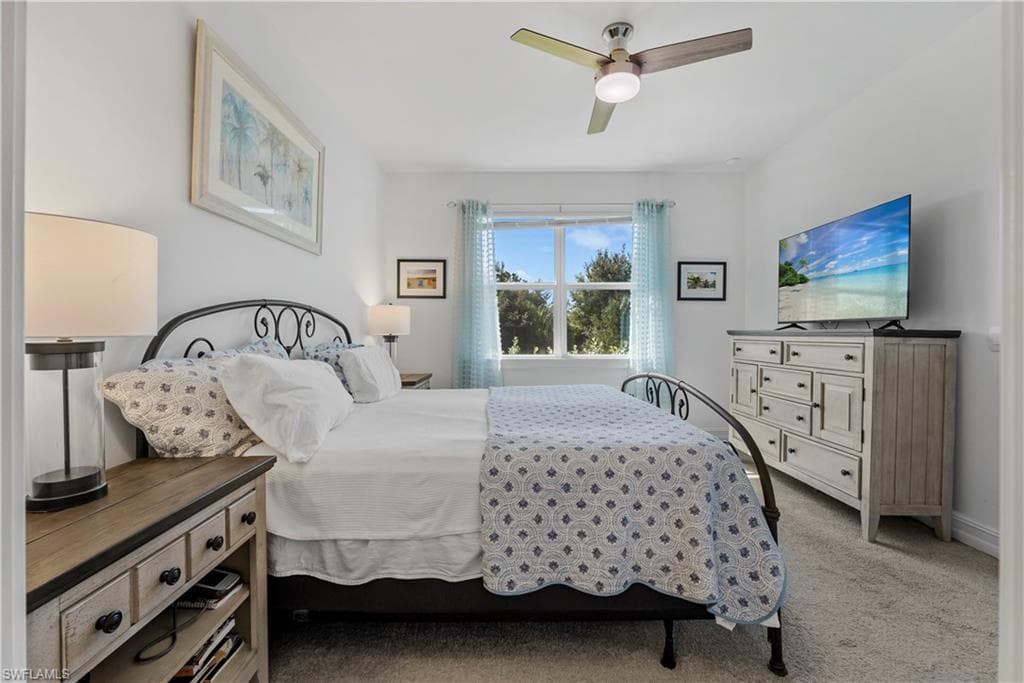 Bright, airy bedroom featuring a wrought iron bed frame, ceiling fan with integrated lighting, wood-finish nightstands with drawer storage, and a wood-finish dresser with cabinet doors