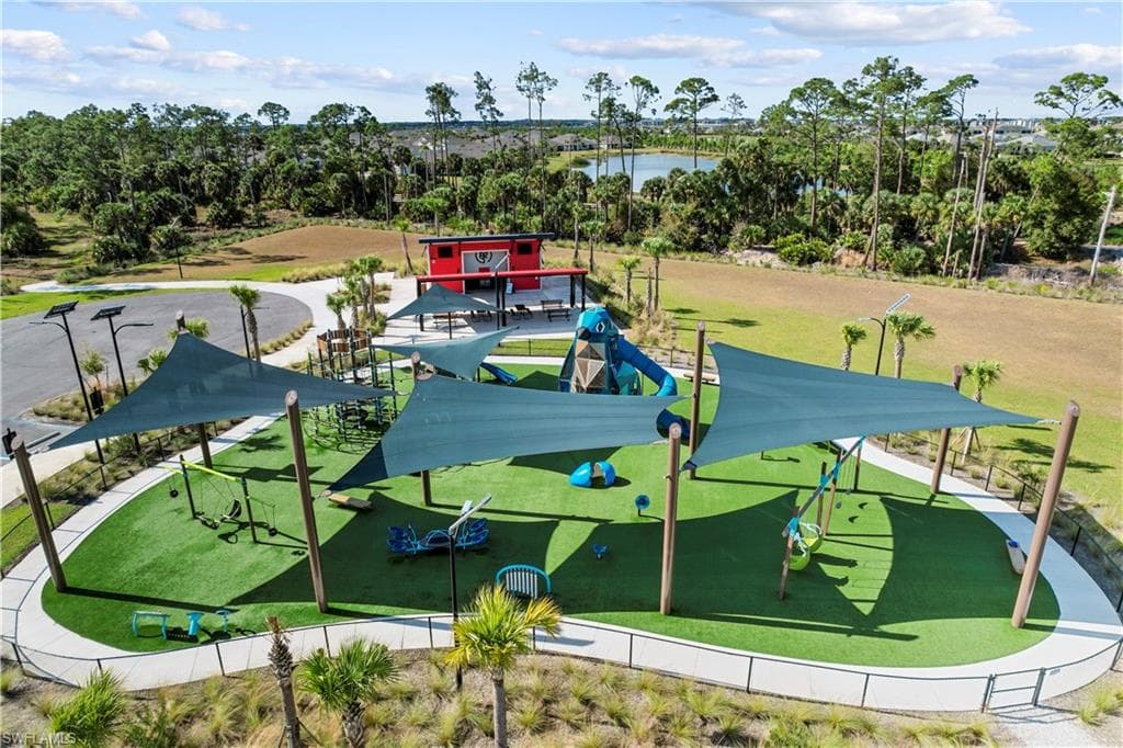 Community playground featuring multiple play structures, artificial turf surfacing, shade sails, and perimeter fencing
