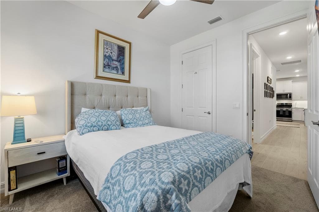 White walls with a ceiling fan, a tufted headboard, and a white nightstand with a drawer