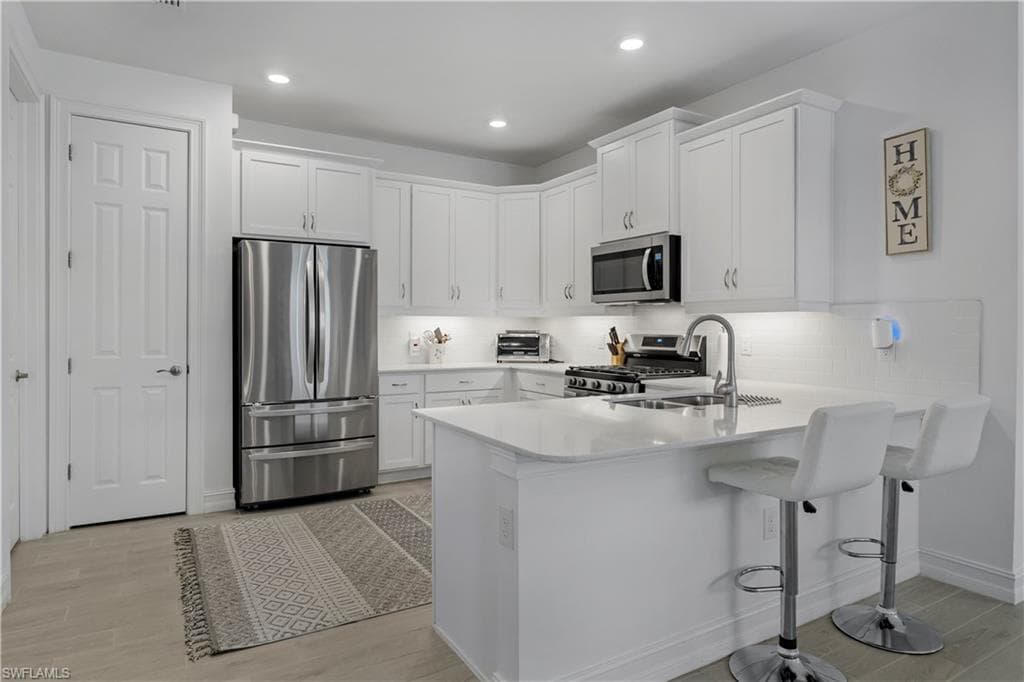 Kitchen featuring white cabinetry, stainless steel appliances, white countertop island with sink, and light wood-finish flooring