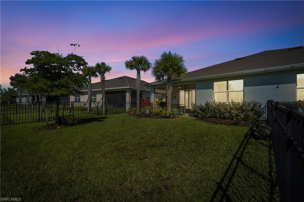 Expansive backyard with manicured lawn, mature landscaping including palm trees and established shade trees, black metal perimeter fencing, and covered patio structure