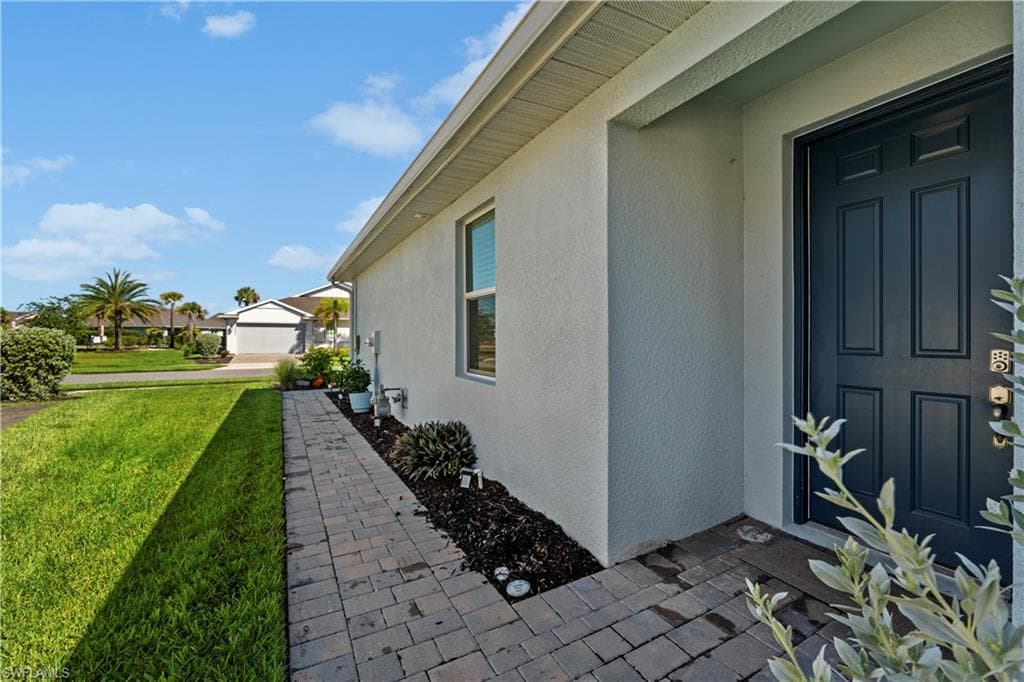Stucco exterior with a paneled entry door, paver walkway, and well-maintained landscaping