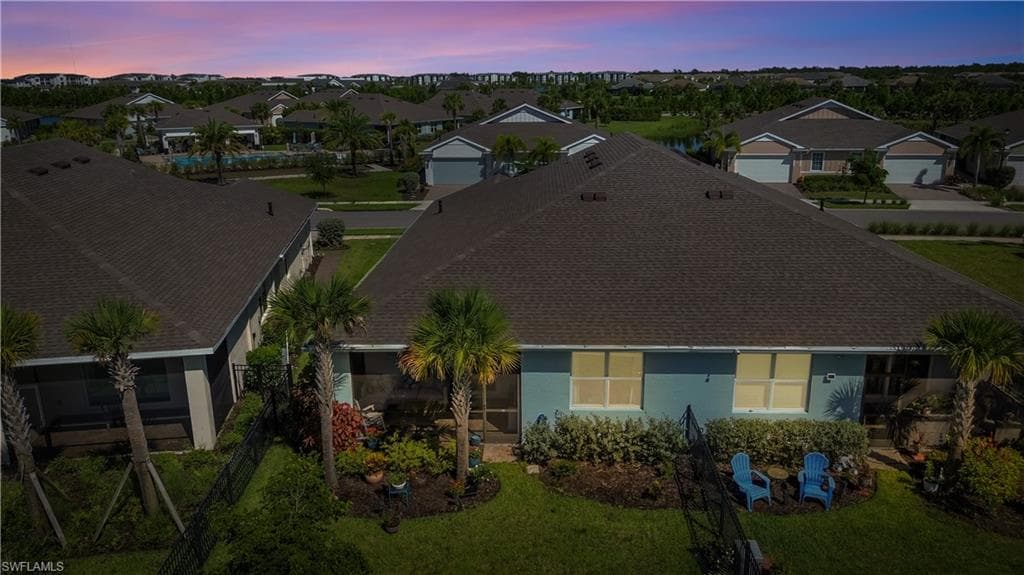 Elegant single-story residence featuring a dark architectural shingle roof, large picture windows with yellow-toned frames, and mature landscaping including palm trees and established plantings