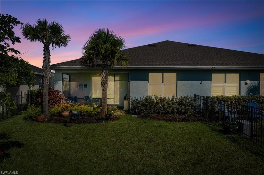 Rear exterior featuring a covered patio, landscaped garden beds, and mature palm trees