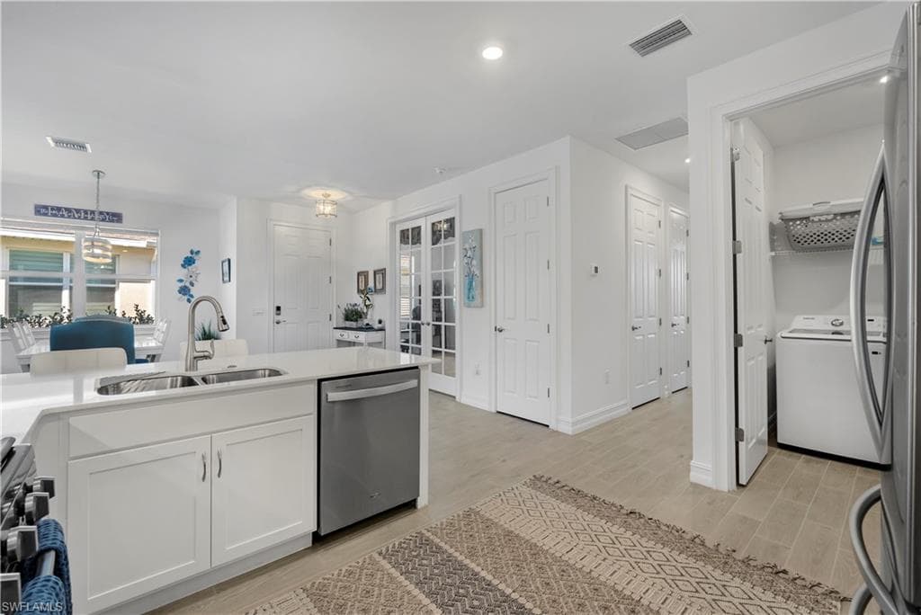 Kitchen island with white cabinetry, stainless steel dishwasher, and a dual basin sink with a high-arc faucet