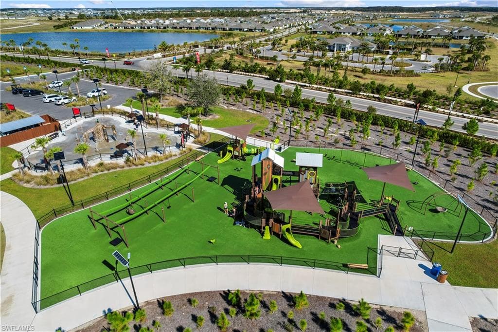 Expansive recreational area featuring a large playground with multiple structures, artificial turf surfacing, shade canopies, and a fenced perimeter
