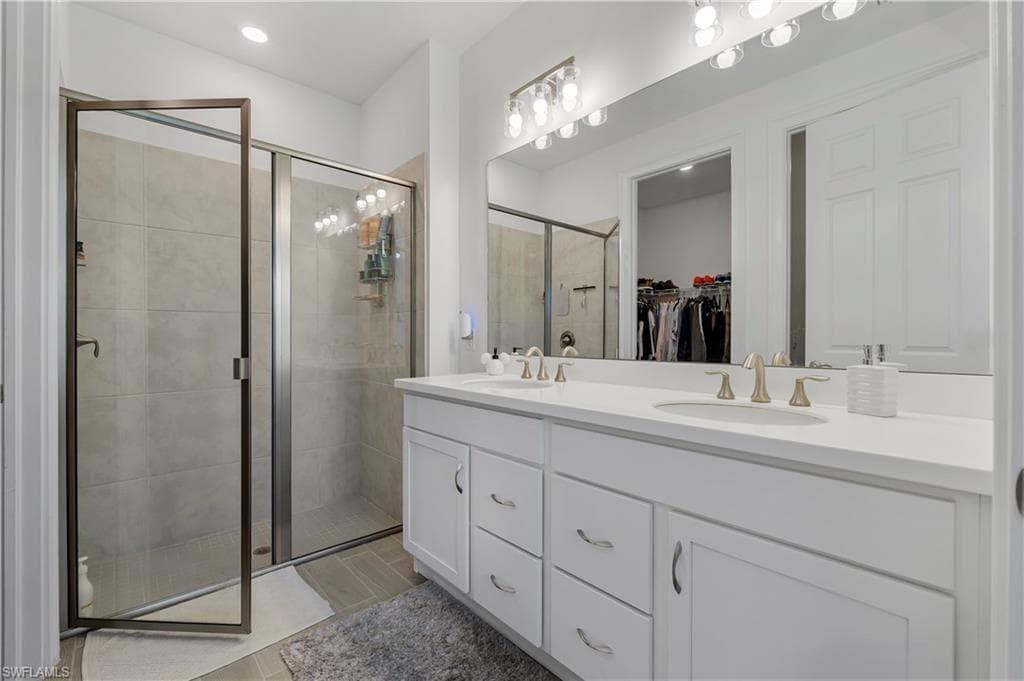 Dual vanity with white cabinetry and integrated sinks, a large frameless mirror, and a tiled shower with a glass enclosure