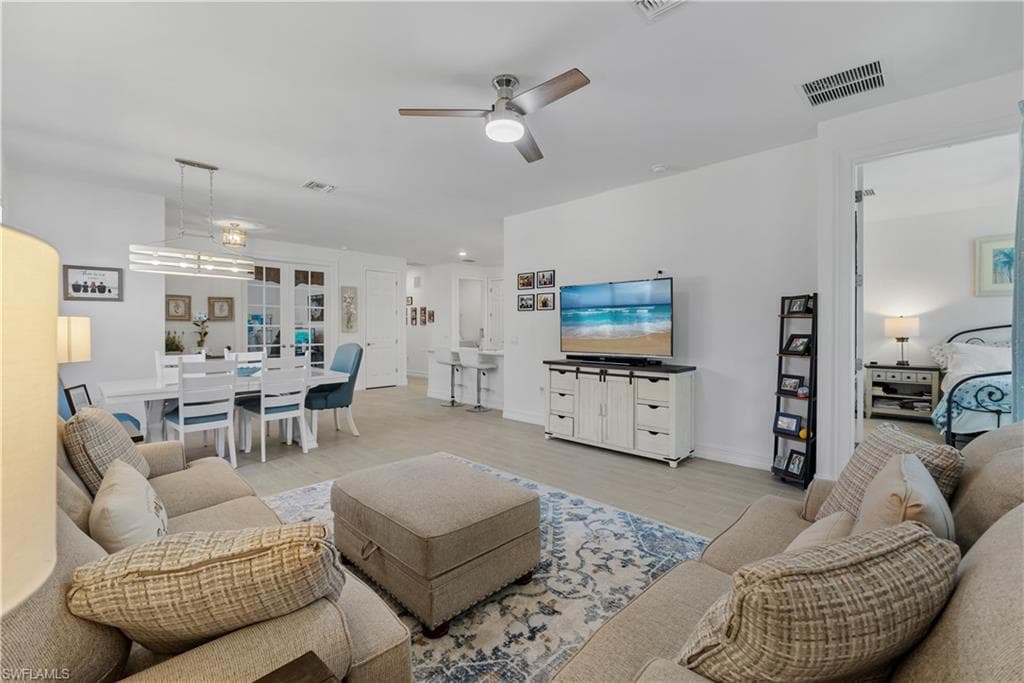 Open-concept living area featuring neutral upholstered seating, a wood-finish flooring throughout, and a ceiling fan with integrated lighting