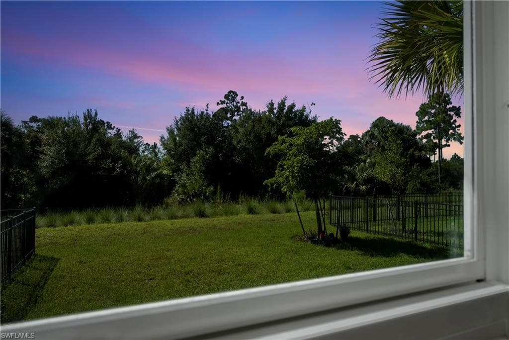 Expansive backyard with manicured lawn, mature tree canopy, and black metal fencing