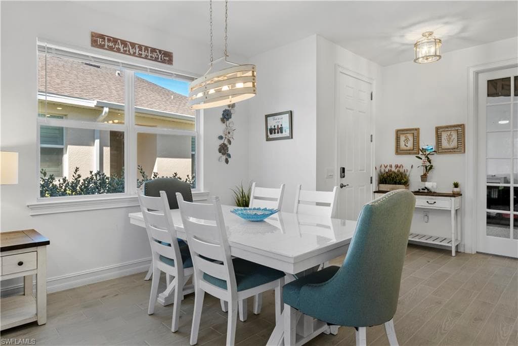 Spacious dining area featuring a large window, a modern chandelier, light-toned wood-finish flooring, and a glass-paned door