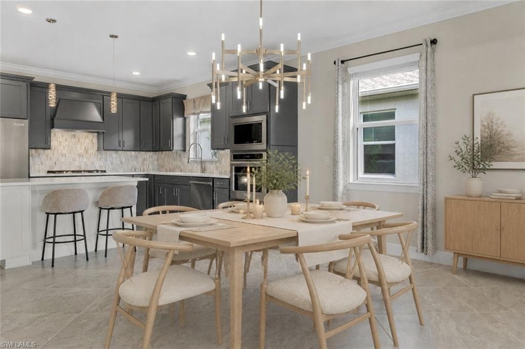 Open-concept dining area with a modern chandelier, light wood-finish flooring, and a kitchen featuring dark cabinetry, stainless steel appliances, and a tiled backsplash