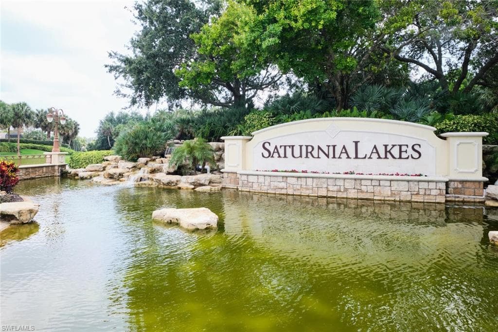 Community entrance signage with stone detailing, a water feature, and mature landscaping