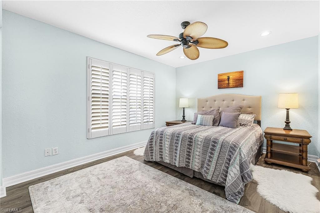 Wood-finish flooring with light-colored walls, white plantation shutters, and a ceiling fan