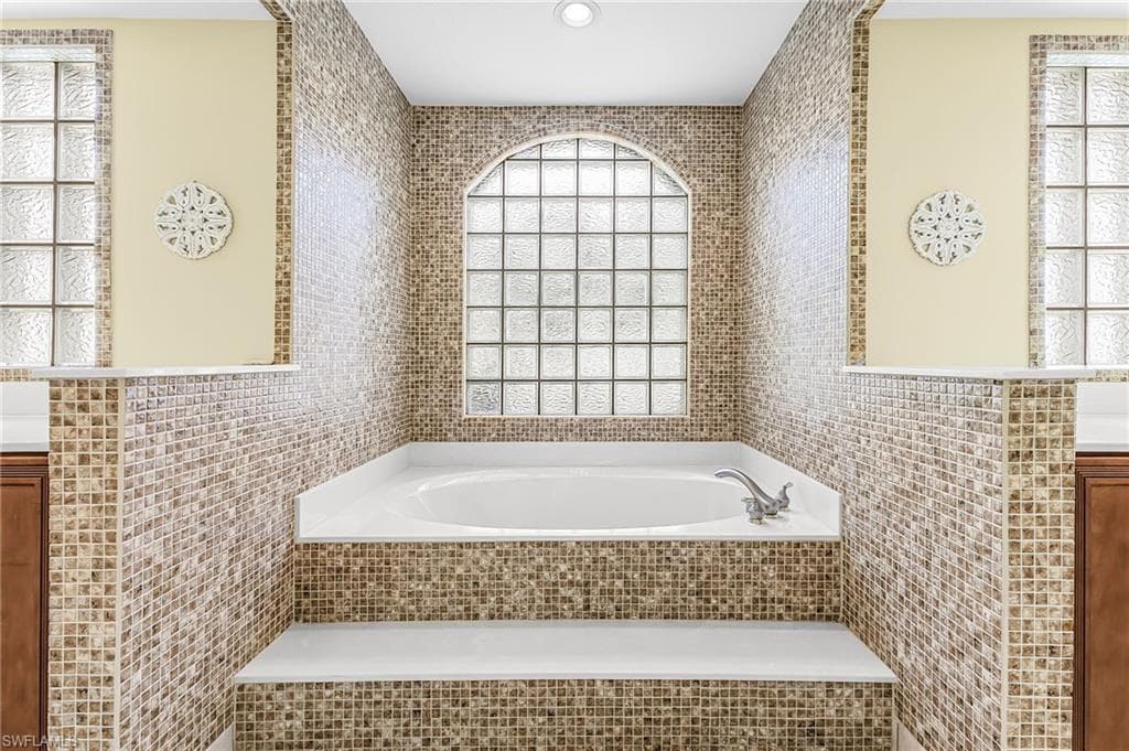 Built-in tub with mosaic tile surround, arched glass block window, and dual privacy windows