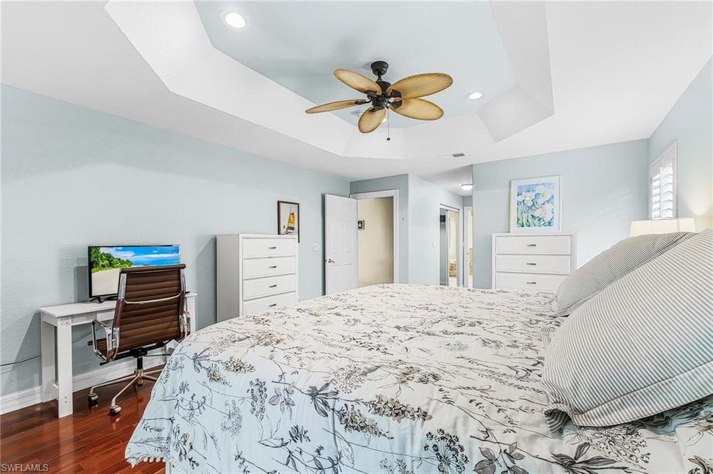 Tray ceiling with recessed lighting, ceiling fan, rich wood-finish flooring, and plantation shutters