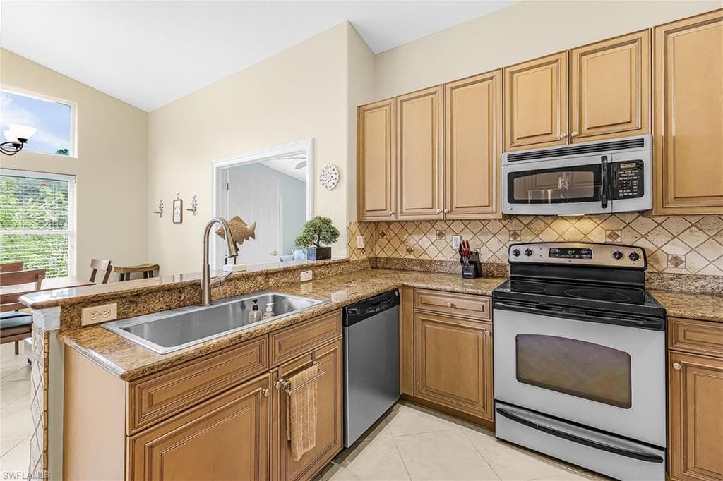 Kitchen featuring wood-finish cabinetry, granite countertops, tile backsplash, and stainless steel appliances