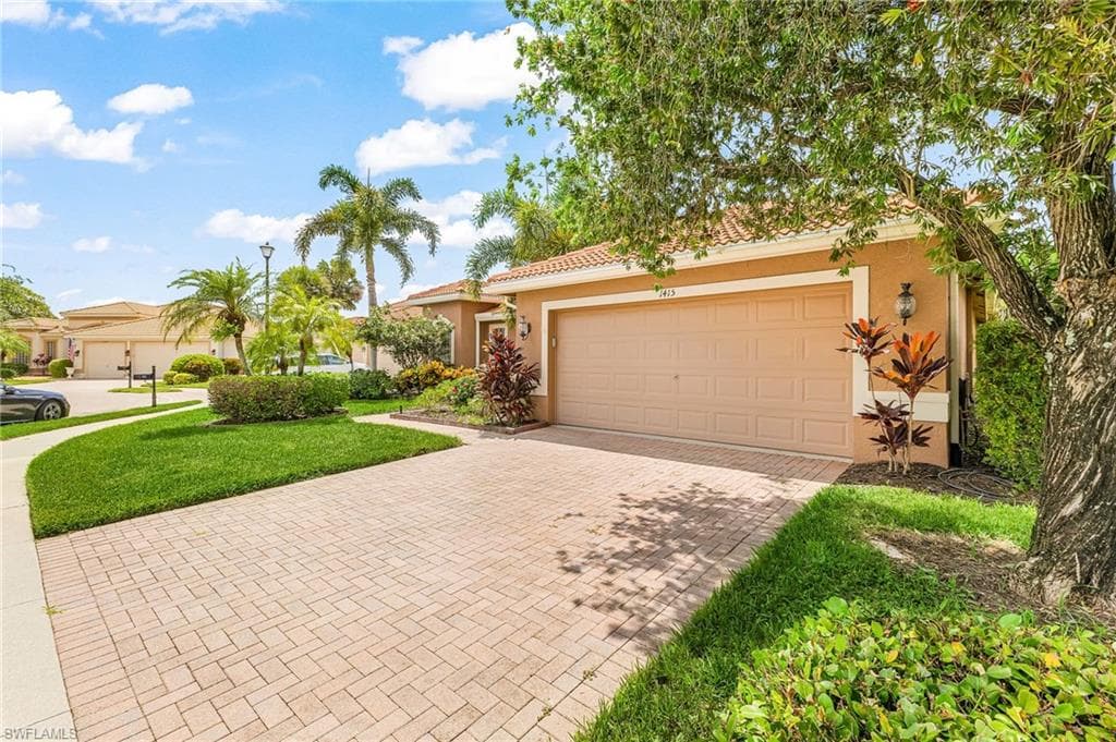 Brick paver driveway leading to a two-car garage, complemented by mature landscaping and a well-maintained lawn