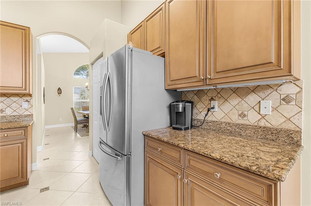 Kitchen with wood cabinetry, stainless steel refrigerator, granite countertops, and tiled backsplash