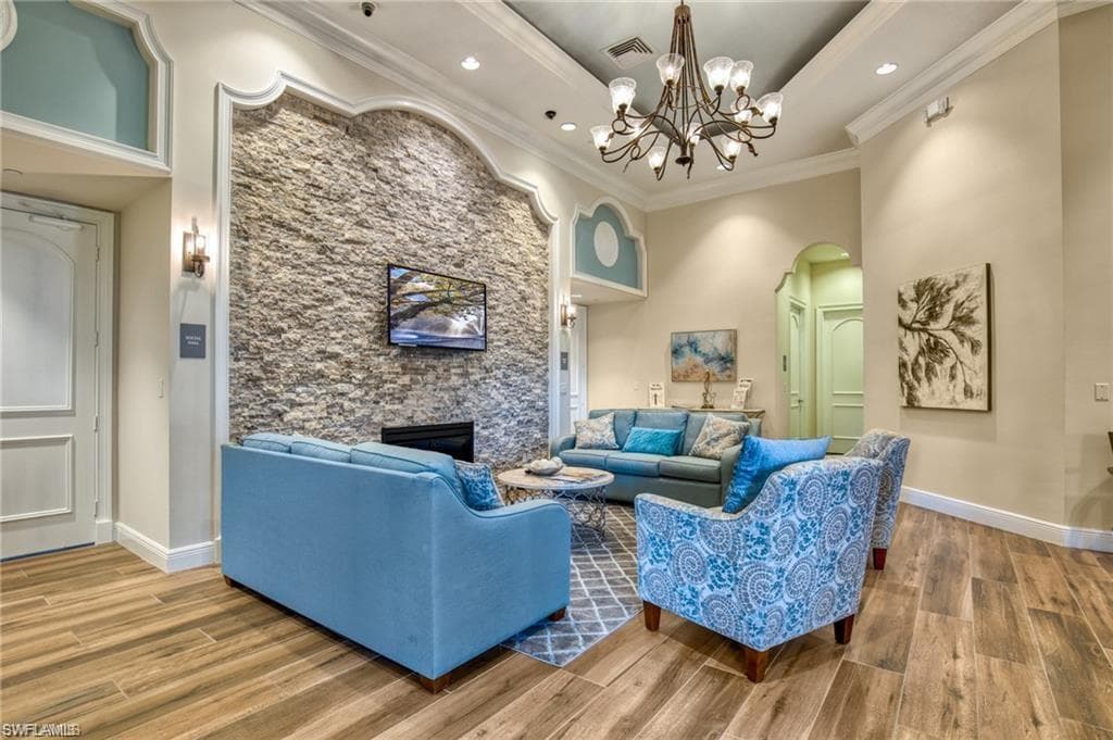 Wood-finish flooring, stone accent wall, crown molding, built-in fireplace, and a decorative chandelier