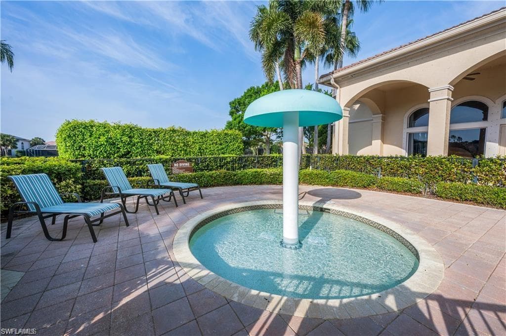 Paved patio with a circular water feature, surrounded by mature hedges and an arched building facade