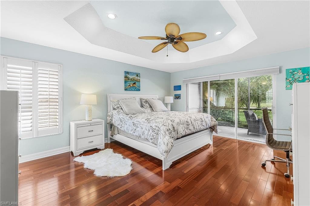 Tray ceiling with recessed lighting and a ceiling fan, wood-finish flooring, sliding glass doors to a screened patio, and window with plantation shutters