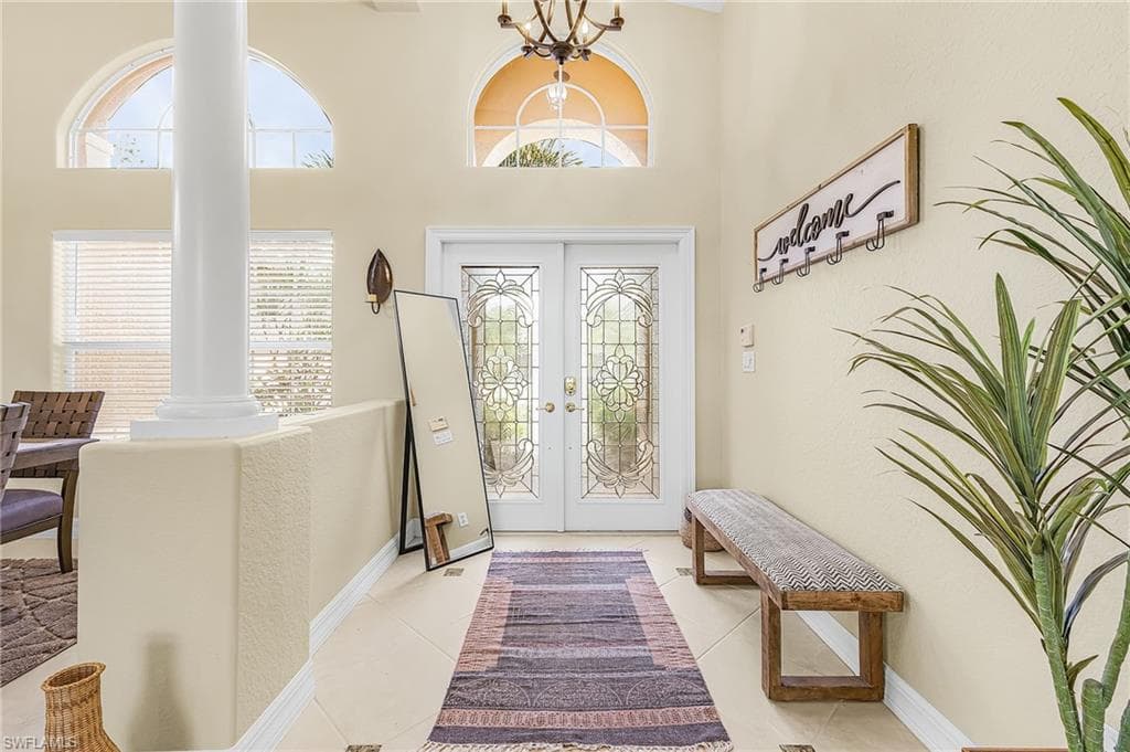 Bright foyer featuring dual glass-paneled doors with decorative muntins, arched transom windows, light-filled spaces with crown molding, and polished tile flooring