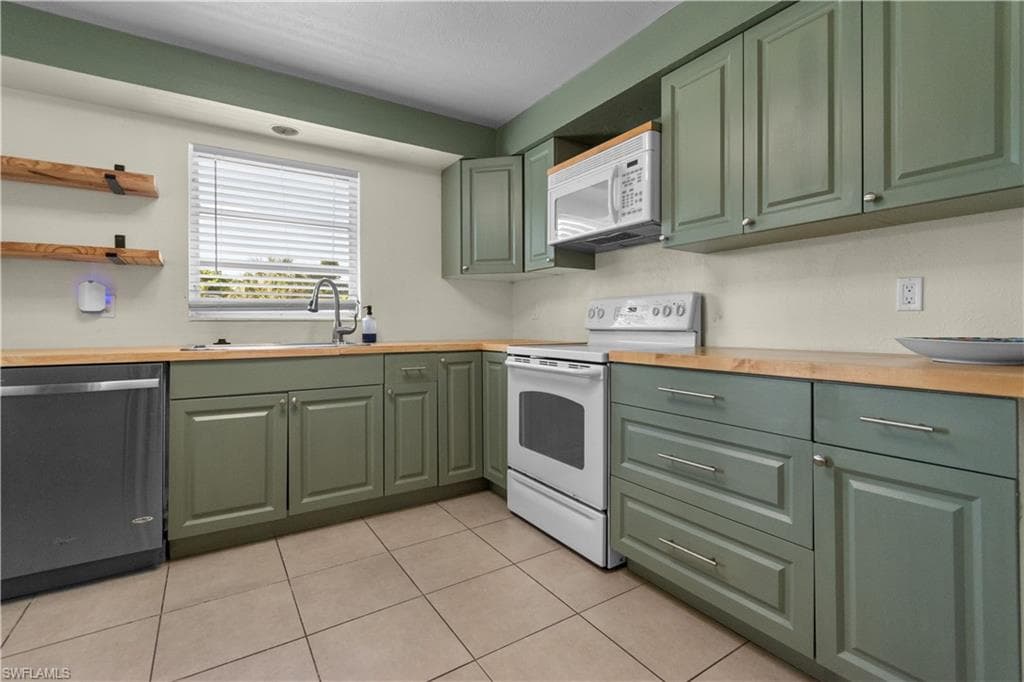 Kitchen featuring wood-finish countertops, green cabinetry with silver-tone hardware, tile flooring, and a stainless steel dishwasher