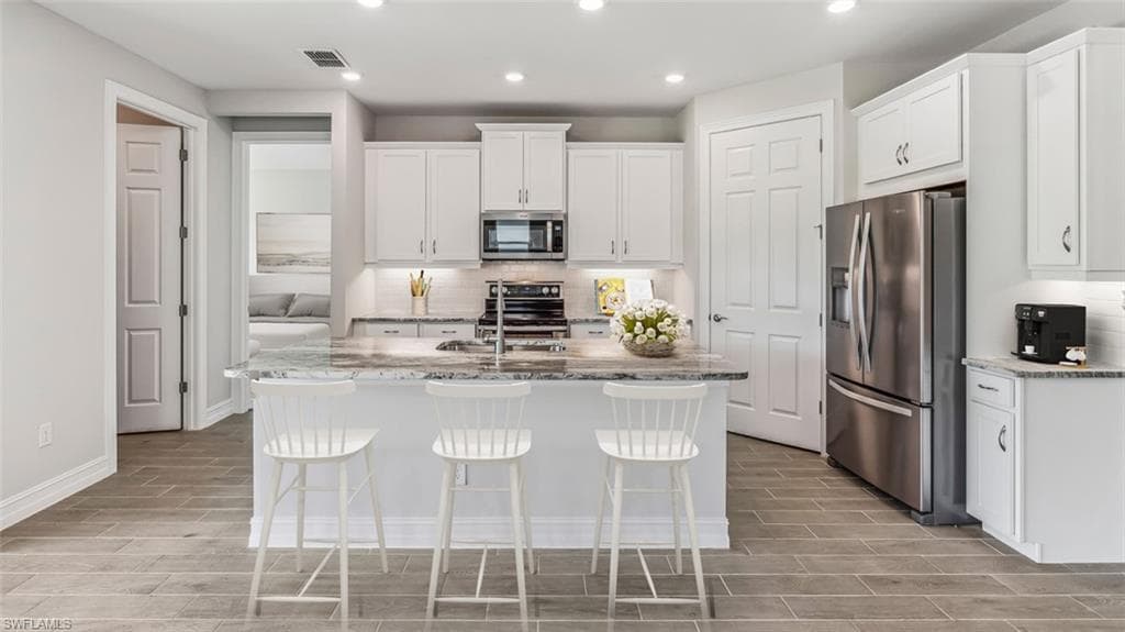 This image is virtually staged. Kitchen with light stone counters, white cabinets, stainless steel appliances, and recessed lighting