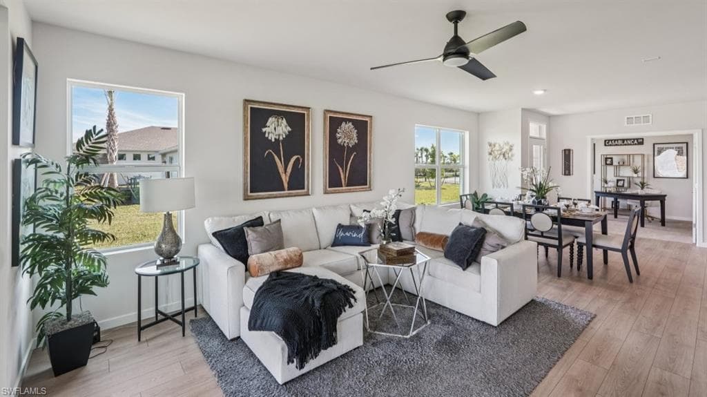 Open-concept living area featuring light-toned walls, wood-finish flooring, and multiple windows
