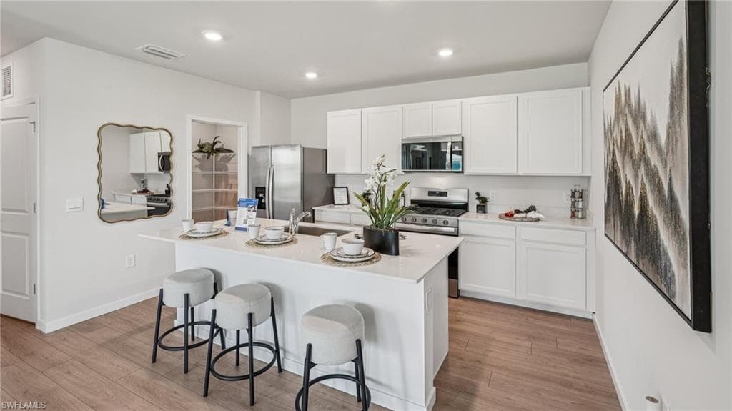 Open-concept kitchen featuring an island with counter seating, stainless steel appliances, white cabinetry, and wood-finish flooring