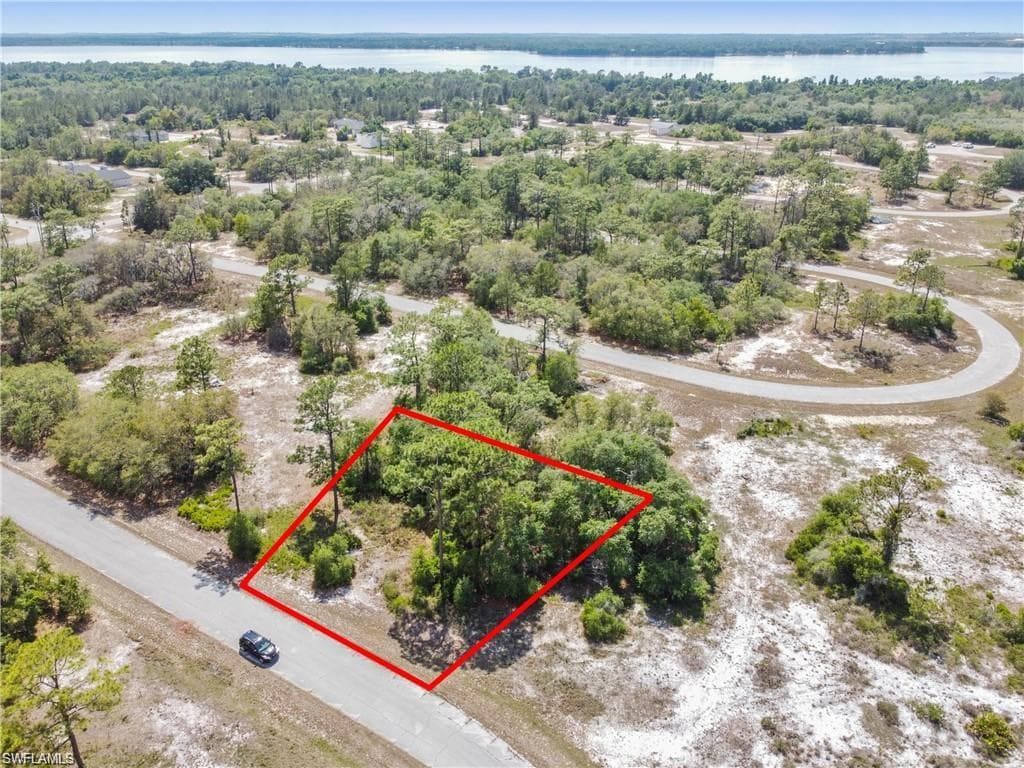 Wooded lot with paved road frontage, surrounded by natural landscaping, and proximity to a large body of water