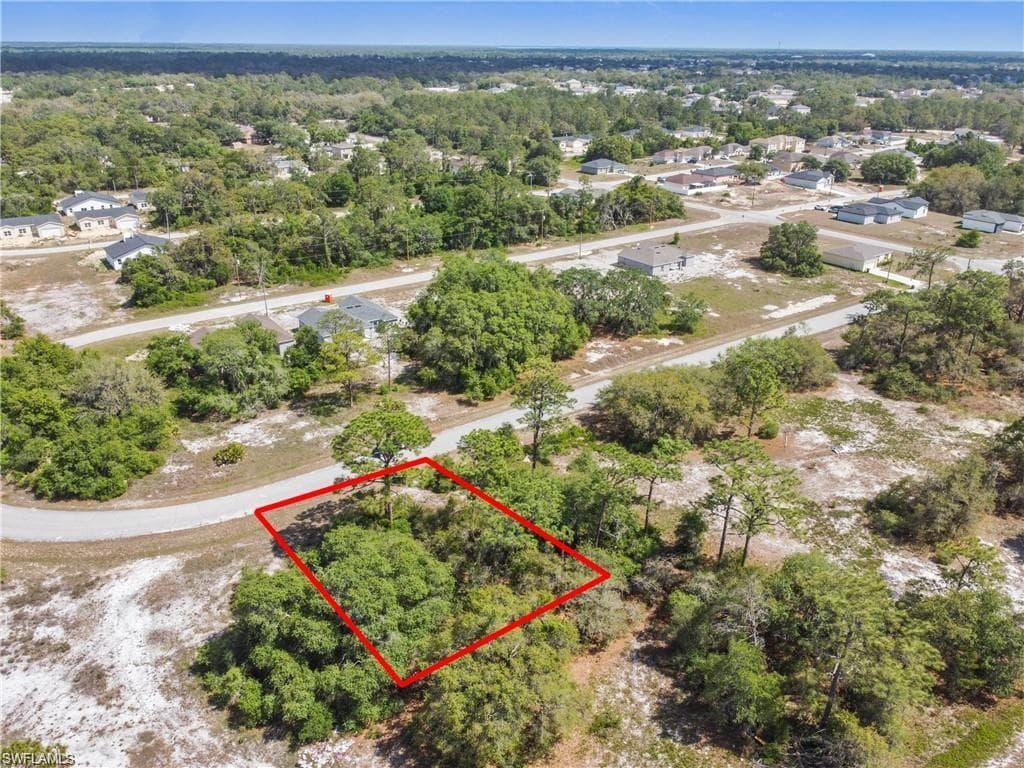 Vacant parcel with extensive natural foliage, featuring surrounding roads and distant residential structures