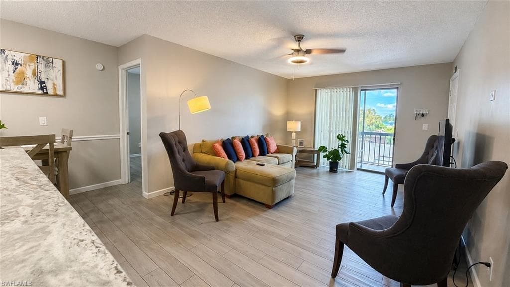 Wood-finish flooring throughout, ceiling fan with integrated lighting, sliding glass door providing balcony access, and two-tone wall paint
