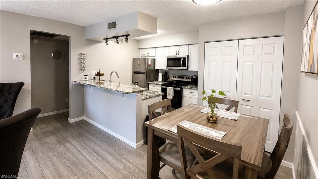 Kitchen with granite countertops, stainless steel appliances, wood-finish flooring, and white cabinetry
