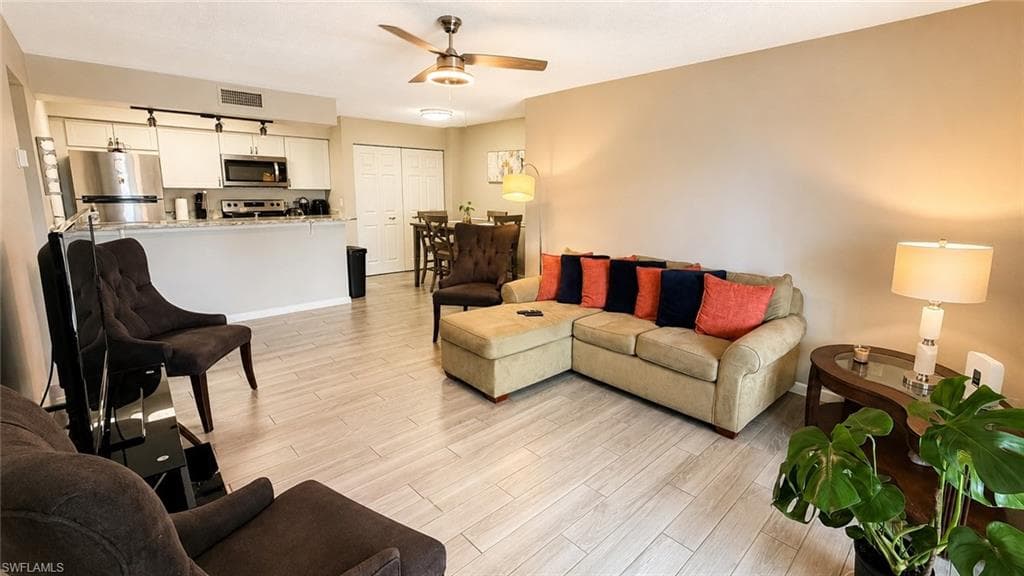 Open concept living area with wood-finish flooring, kitchen island, white cabinetry, and stainless steel appliances