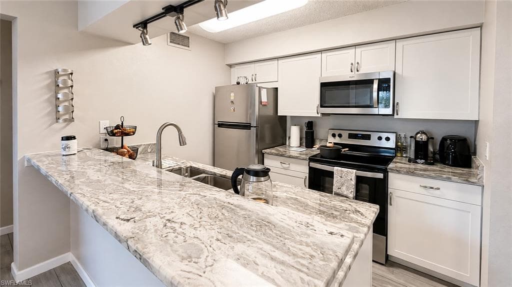 Modern kitchen featuring expansive granite-style quartz countertops with waterfall edge detailing, stainless steel appliances including a gas range and microwave, soft-close white cabinetry, and a polished chrome gooseneck faucet with pull-down spray