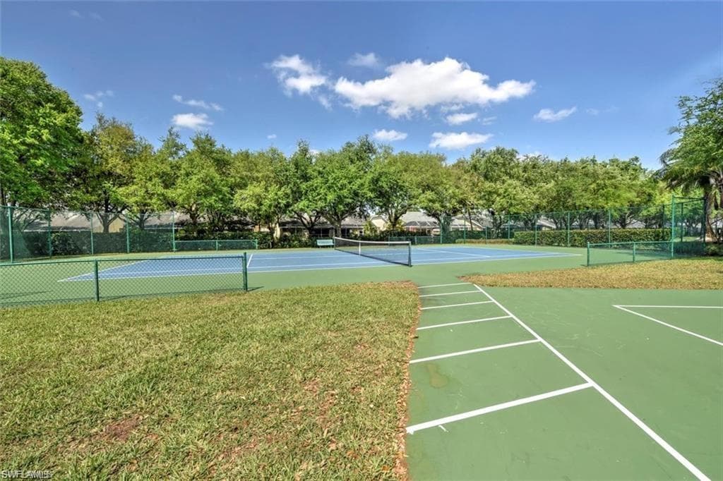 Tennis court with blue playing surface, surrounded by green fencing and mature trees
