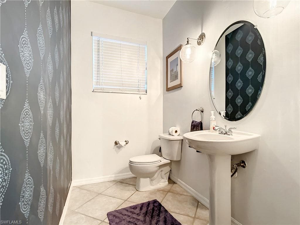 Pedestal sink with chrome faucet, oval wall-mounted mirror, and ceramic tile flooring
