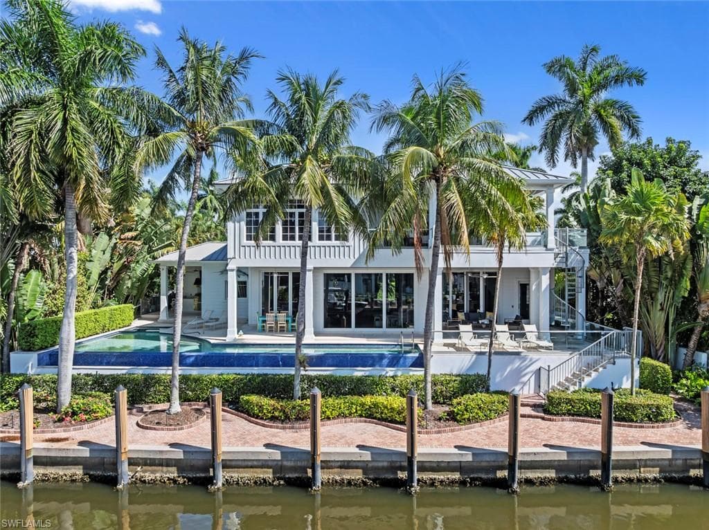 Waterfront residence featuring a private dock, expansive pool, second-story balcony with spiral staircase, and lush tropical landscaping