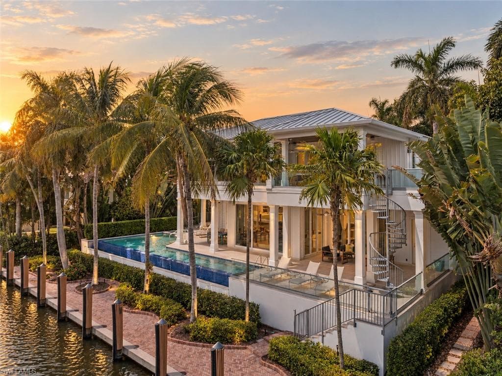 Waterfront residence featuring a private dock, expansive swimming pool, spiral staircase, upper-level balcony with glass railings, and mature palm trees