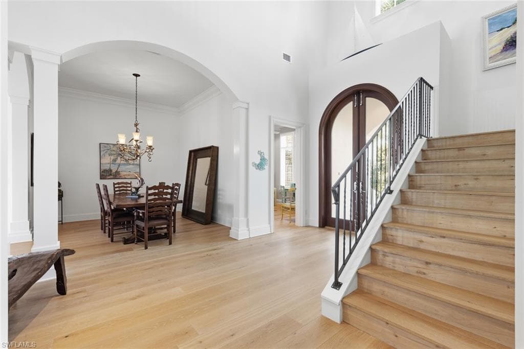 Light wood-finish flooring throughout, prominent staircase with wrought iron balusters, arched entryway, and high ceilings