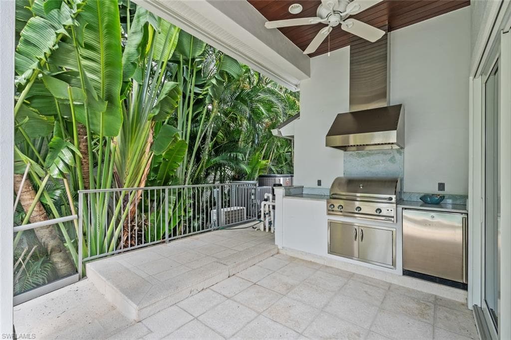 Outdoor kitchen featuring stainless steel grill, range hood, and under-counter refrigerator